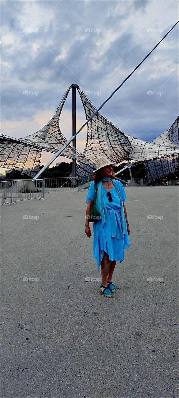 The futuristic design of the stadium for the “1972 Olympics” in “Munich” combined with the antique Greek or Roman inspired couture of our model standing in front of it on a vast plaza creates quite the cosmopolitan look. 2024. Hypnotic Productions