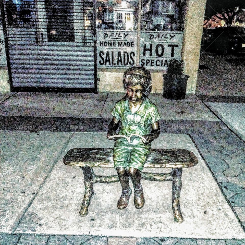 Bronze statue of a little girl reading.