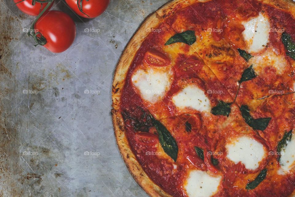 Fresh out of the oven margarita pizza laid flat next to three tomatoes on the vine.