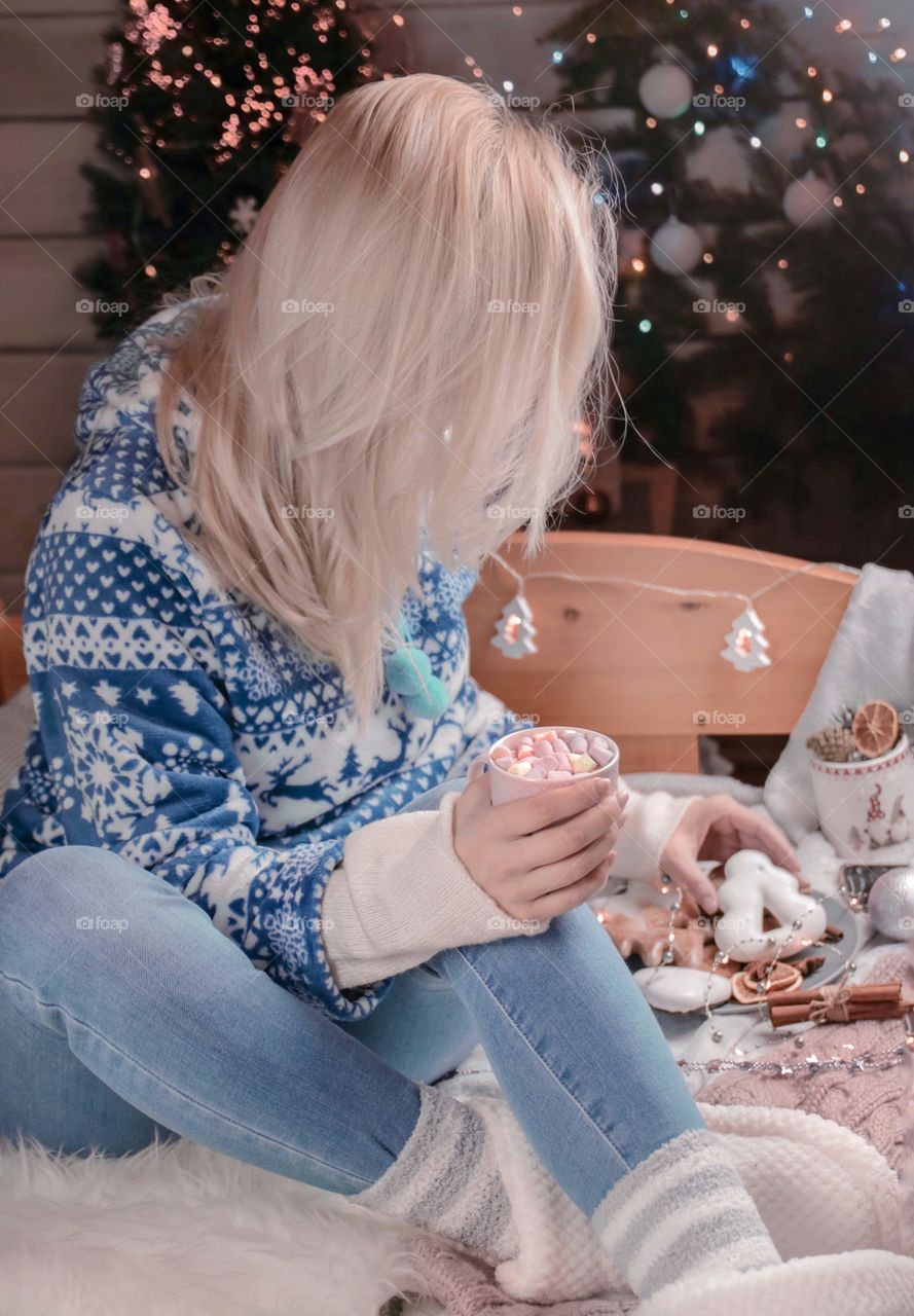 Cup with marshmallows in female hands on a background of Christmas decor