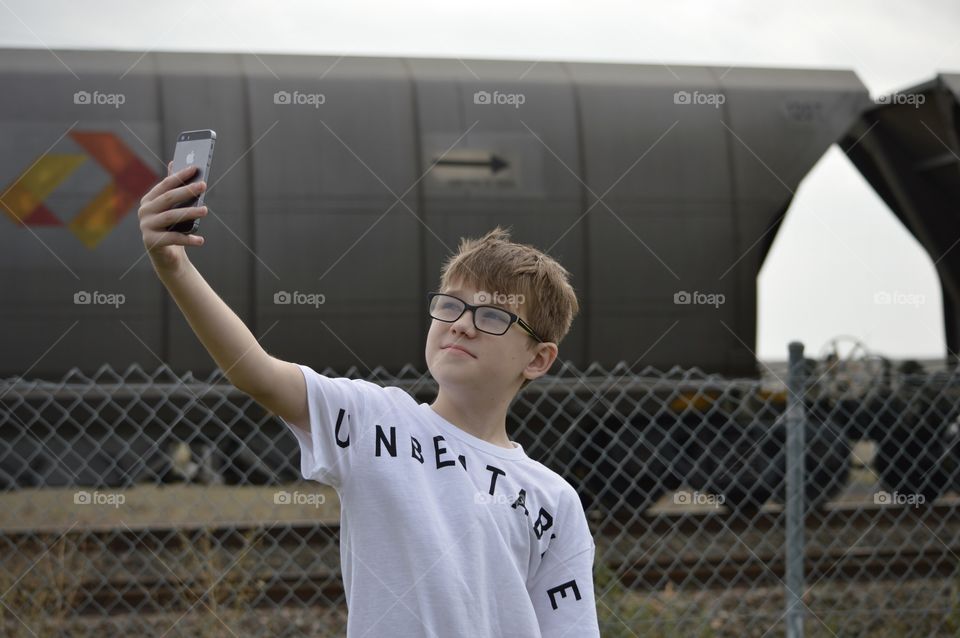 Young boy taking selfie in front of the train him and his nan used to have picnics next to, making memories to add to his picture book as he grows up. Location: in Telarah New South Wales Australia.