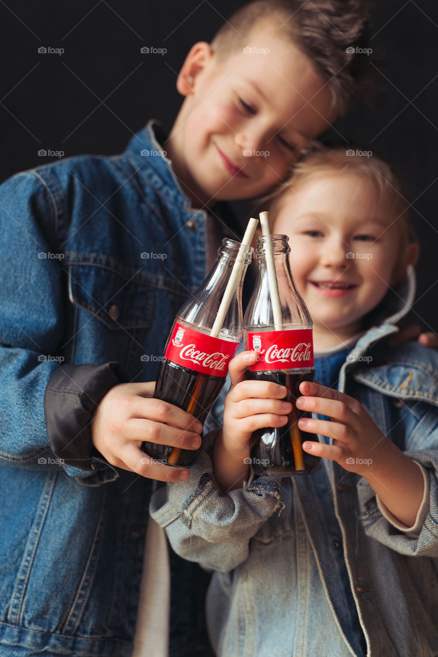 brother and sesira, stay at home, dressed in denim clothes, drink Coca-Cola from bottles through a straw.  beautiful stylish kids