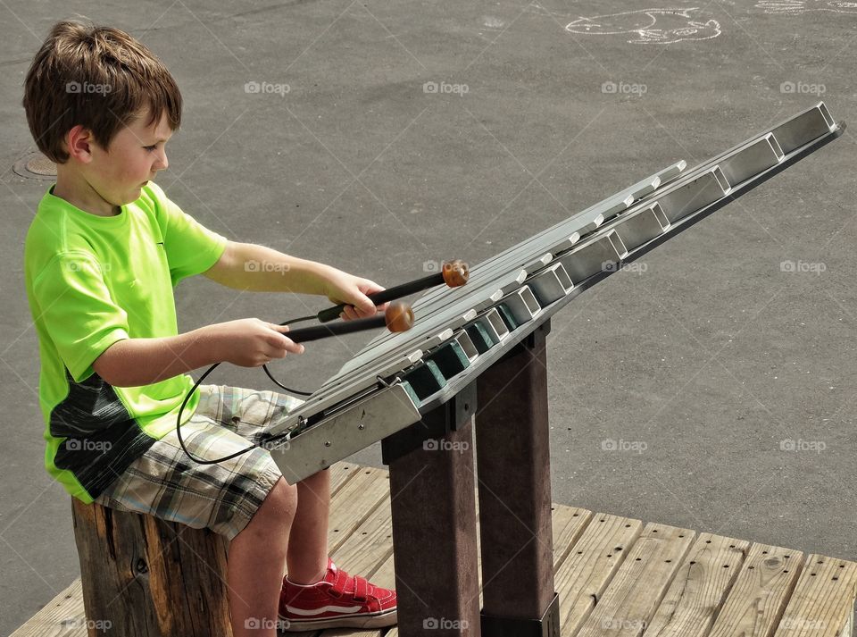 Young Street Musician. Young Boy Playing A Large Metal Xylophone
