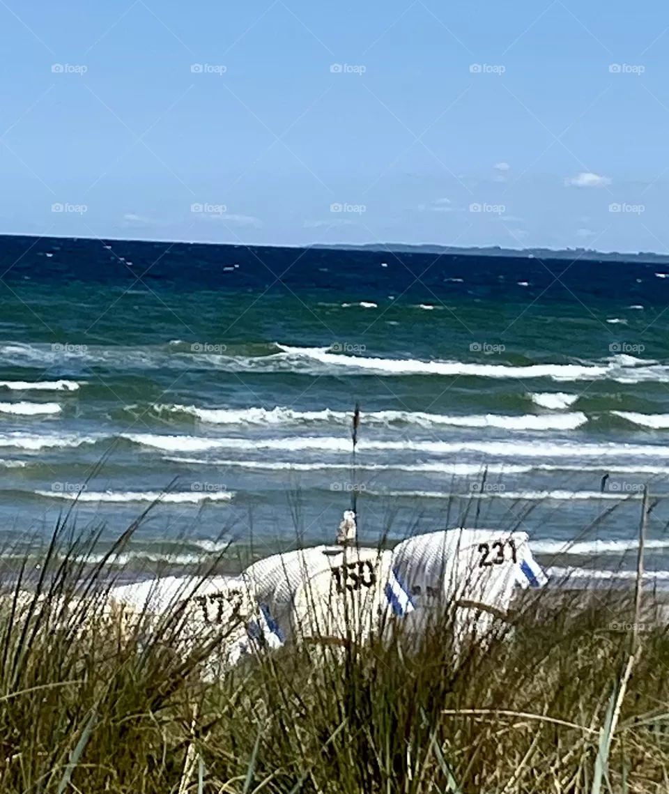 Aufgewühlte Ostsee im Hintergrund gibt hier die perfekte Kulisse für die drei weißen Strandkörbe mit Möwe auf dem mittleren und Strandhafer davor