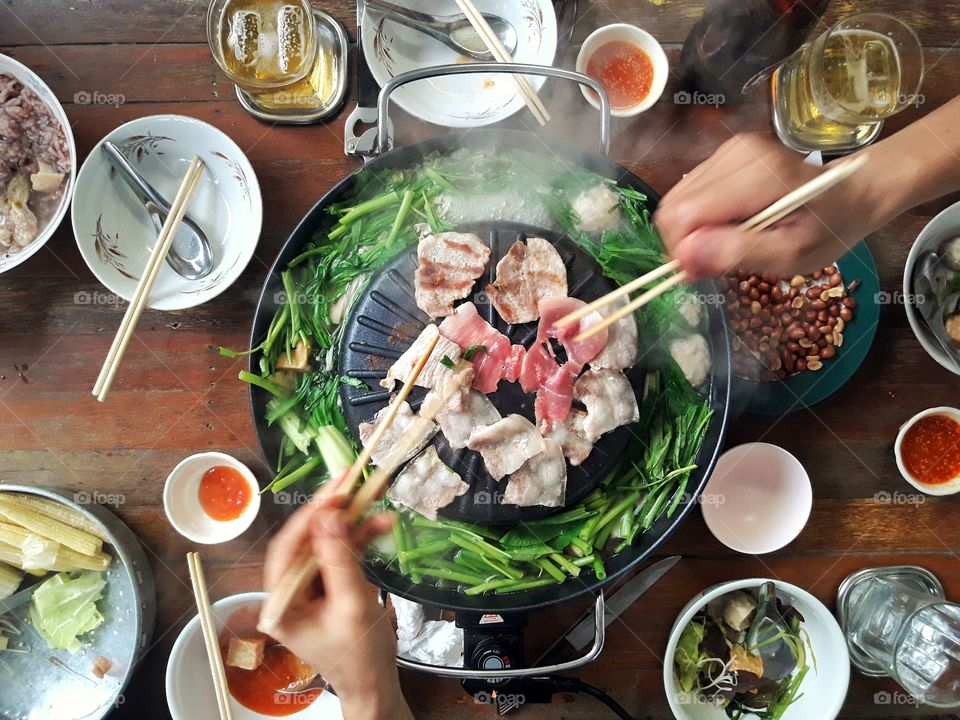 People are eating grilled and boiled foods of various kinds of vegetables.  Along with the delicious tasty dipping sauce that looks very appetizing.
