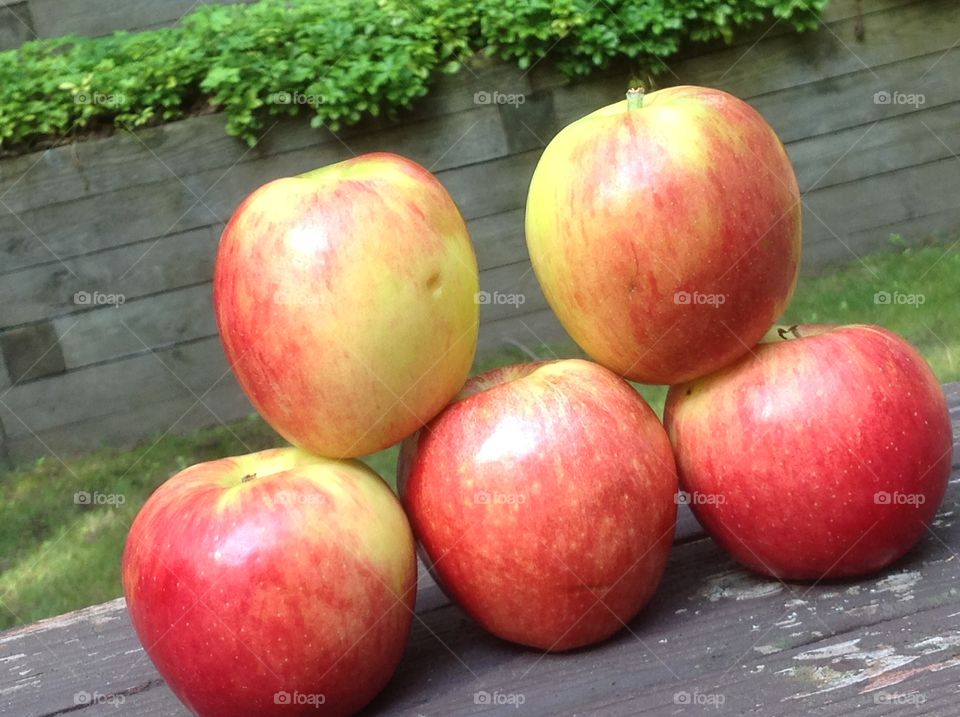 Apples stacked outdoors on wooden bench.