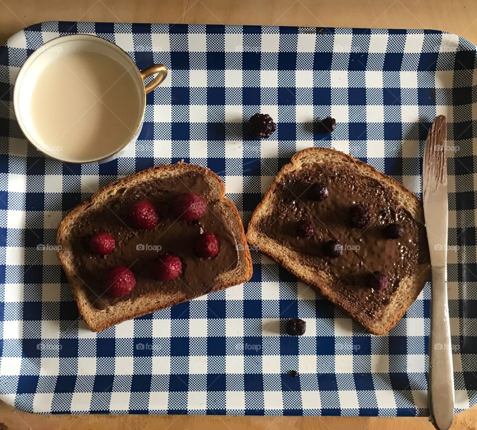 A delicious Nutella sandwich with raspberries and BlackBerries served with a tea cup for lunch on a Blue and white checkered background. USA, America
