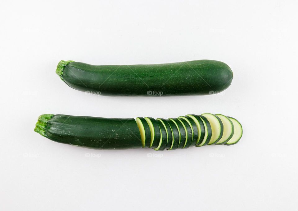 Two green fresh zucchini lying in a row and one of them is cut into skins in the center on a white yon, flat lay close-up. Vegetables concept isolated
