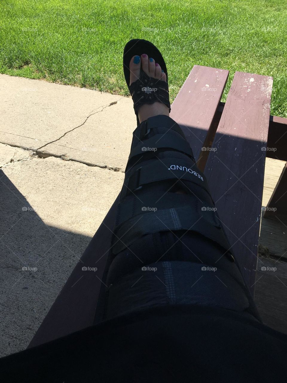 Leg braced leg, with sandled foot, sitting on a bench, leg extended and elevated 