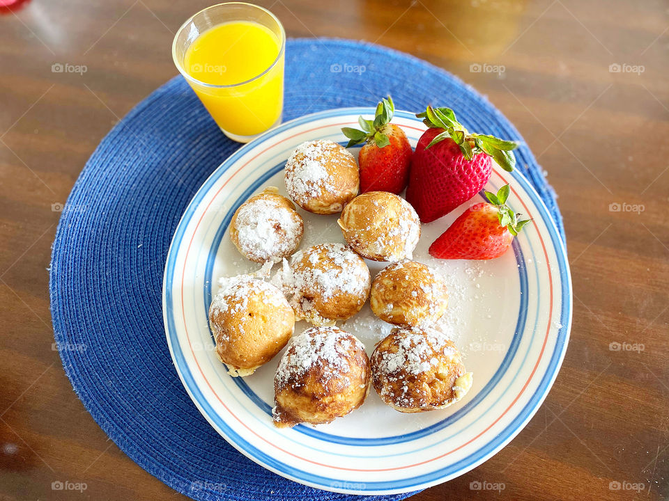 Danish Ebelskiver pancake ball holiday breakfast with powdered sugar, red strawberries, mango juice, on circular plate