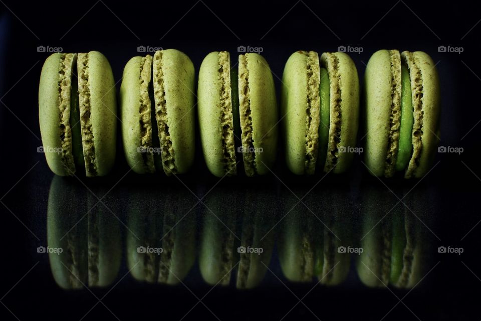 Five green macaroon cookies on a black background