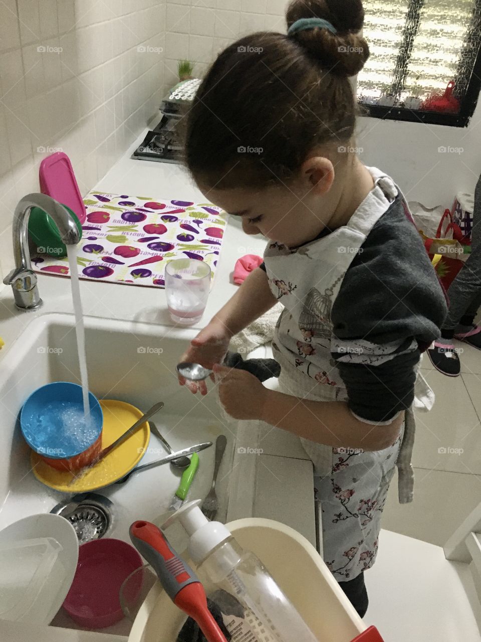 A girl uses a chair to help parents wash dishes