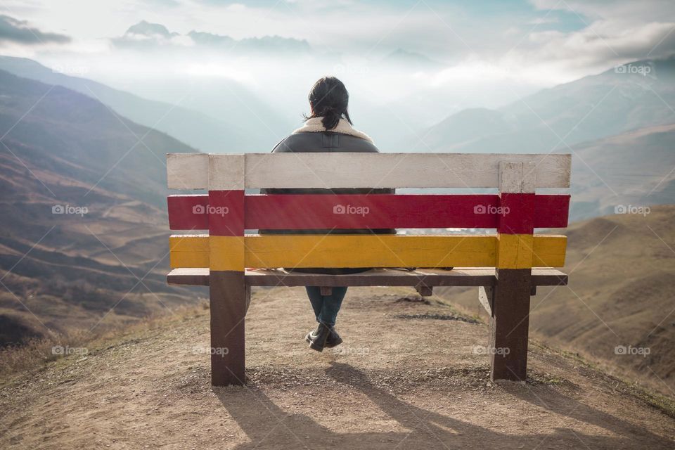 Woman sitting on a bench and looking at mountain . Back view