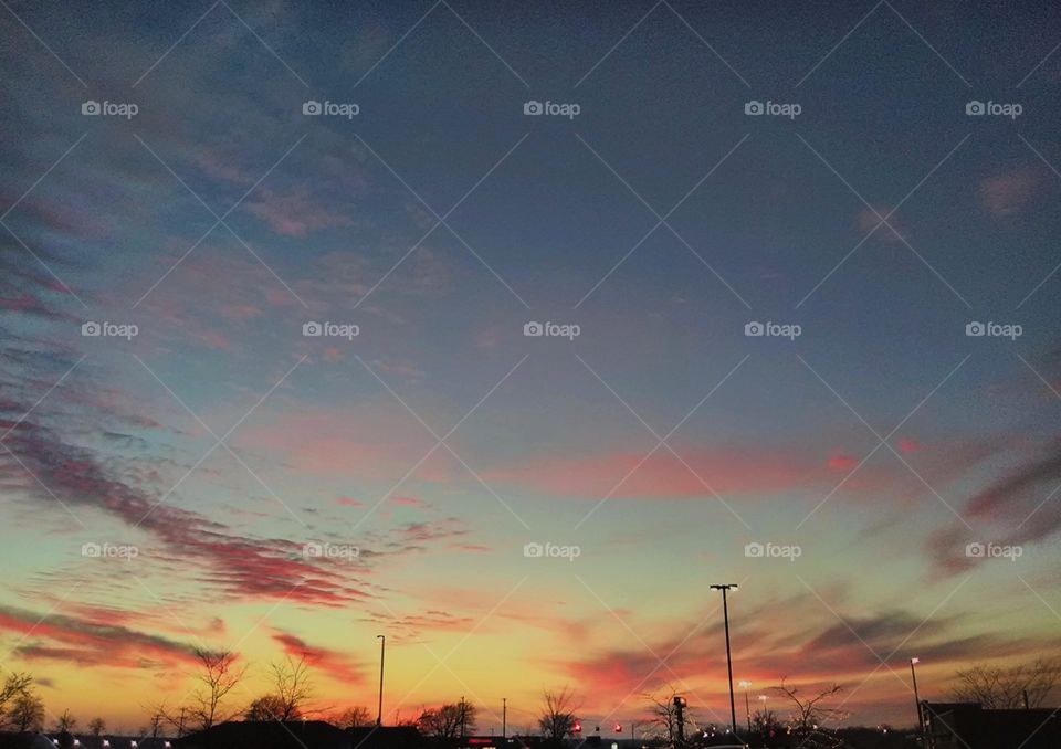huge sky with wispy pink and purple clouds lit by sun set above a parking lot