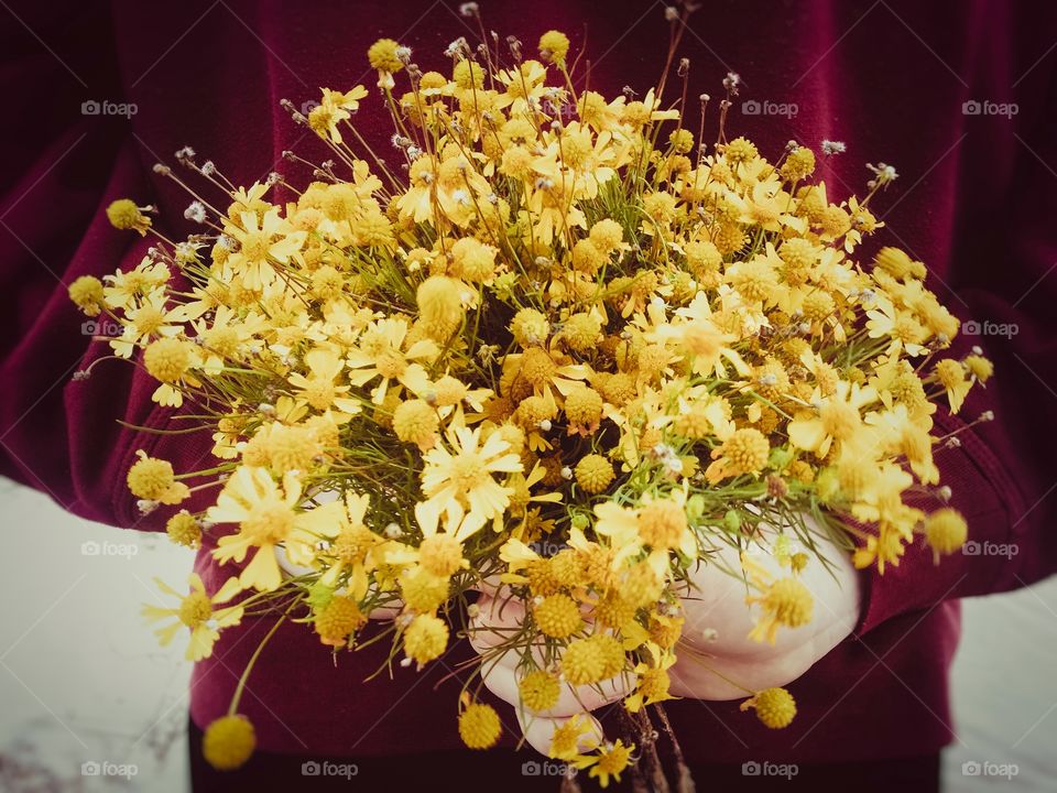 A man holding a bouquet of yellow wildflowers behind his back wearing a dark red shirt