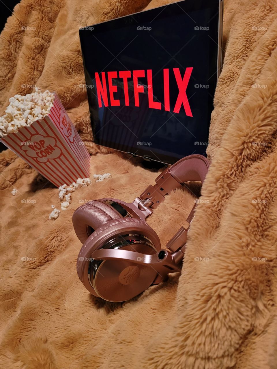 Laptop computer screen ready to watch Netflix for a fun, cozy, and relaxing night with popcorn as a snack, on soft bed blanket in room, with pink headphones