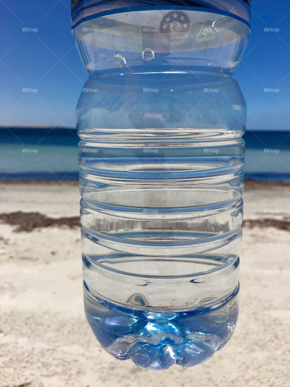 View of remote pristine tropical ocean and summer sky through a plastic bottle of spring water 