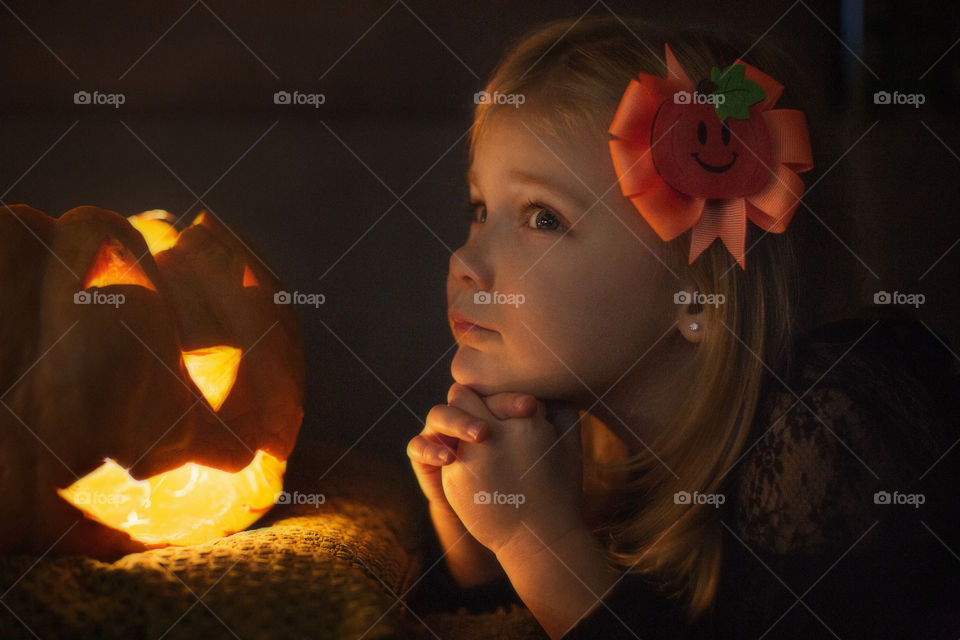 little girl waiting for Halloween, sitting next to a pumpkin head