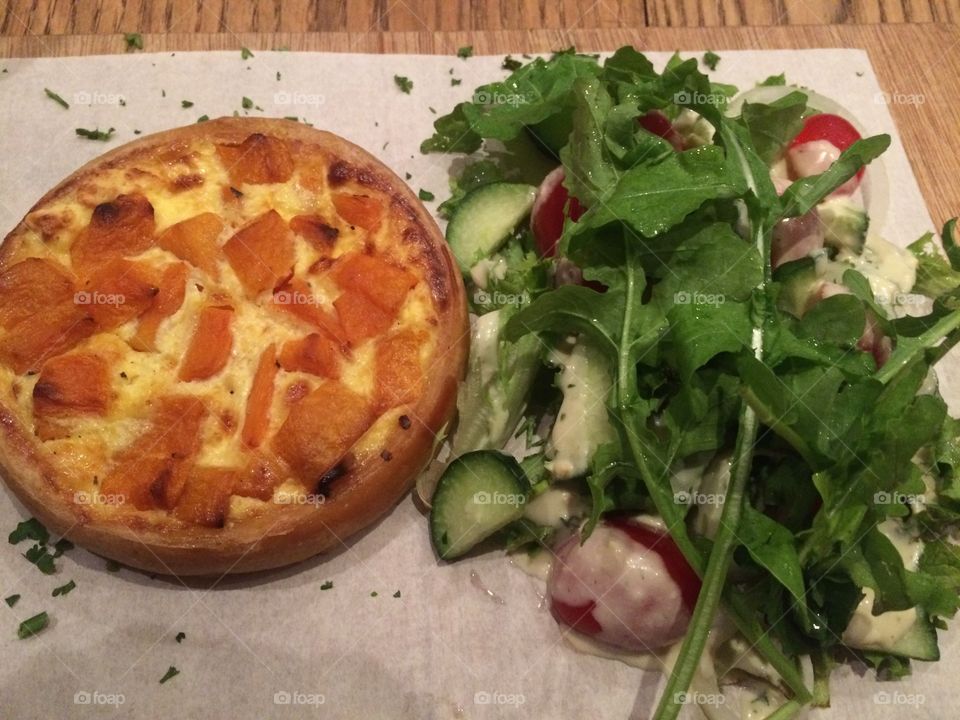 Butternut and feta quiche served with Greek side salad on a wooden board at a restaurant 