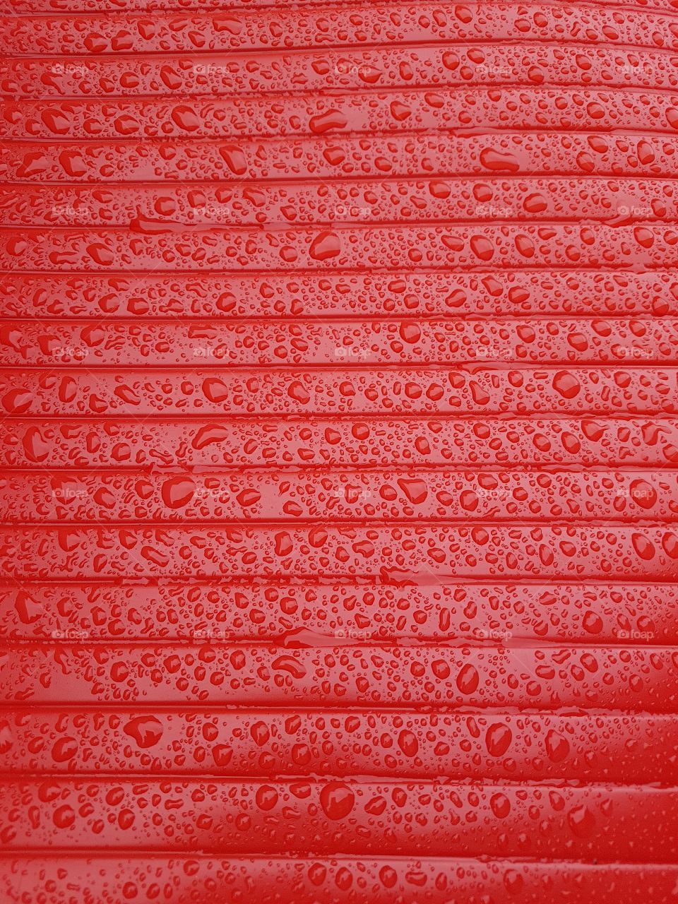 Close up of water droplets on a wet shiny plastic surface red with horizontale lines parallele