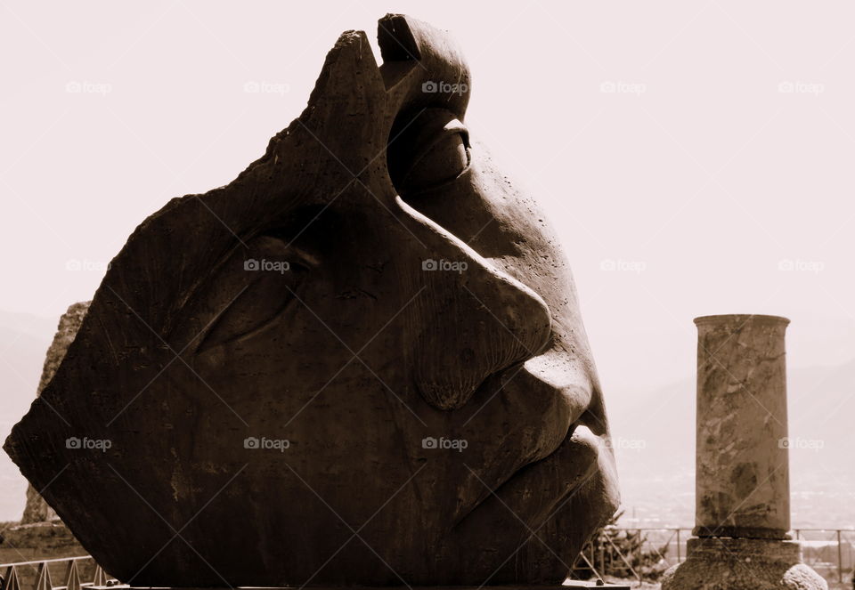 mitoraj face sculpture near a pompeian column