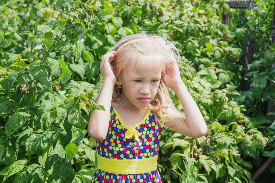 Little beautiful girl stands near a raspberry bush