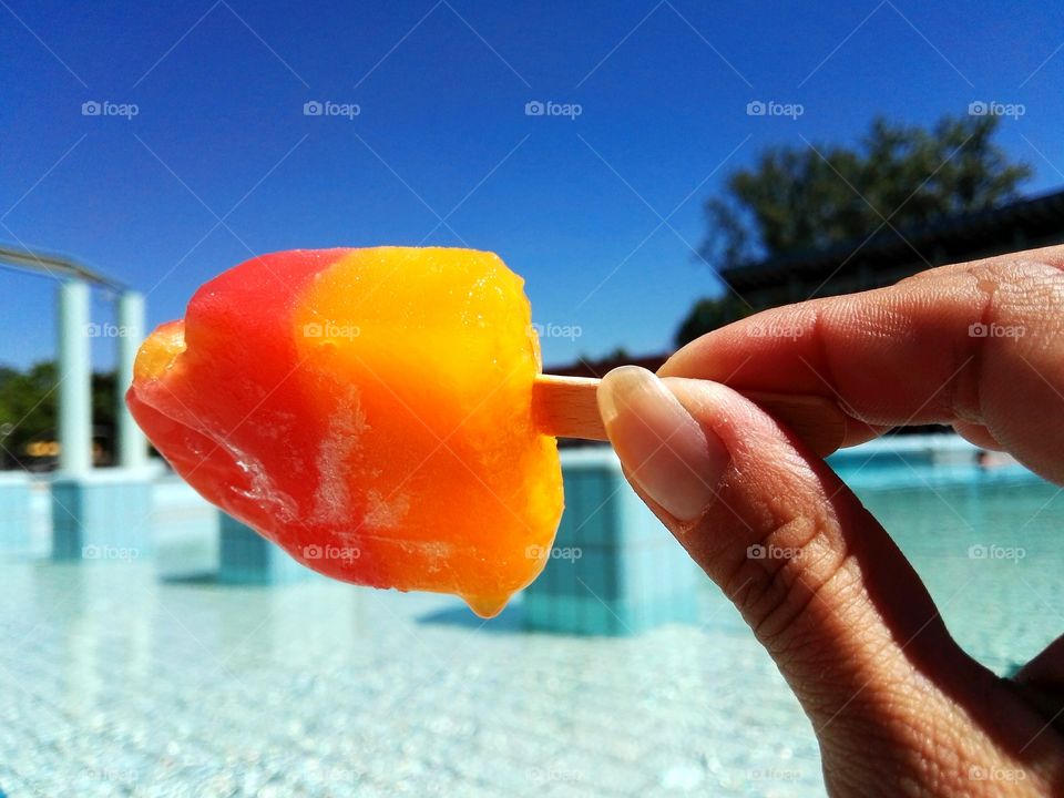 Person holding popsicle stick near swiming pool