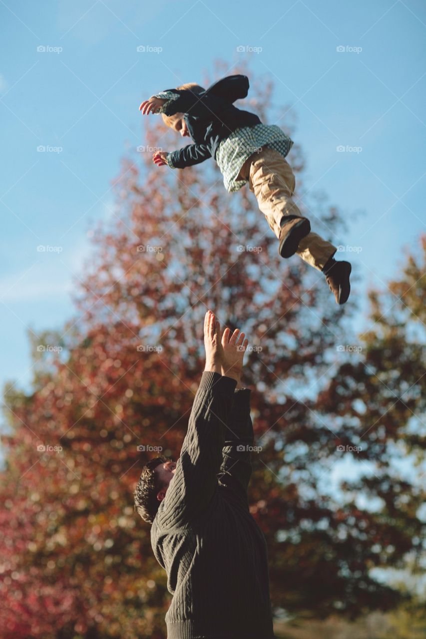 Child being thrown high in the air on a fall day. Father tossing boy son in the air with foliage in background 