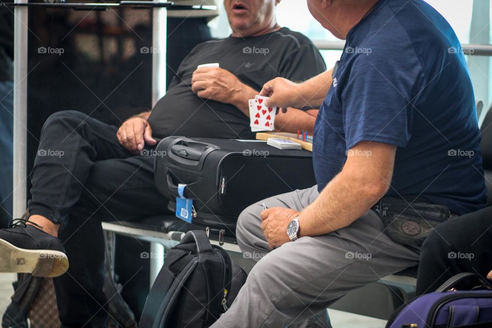 Elder men are having fun playing cards in the airport waiting for their flight