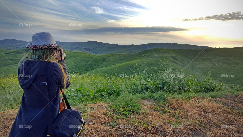 lady holding dslr camera, taking a photo of the hills in spring, carrying an instax camera and camera bag