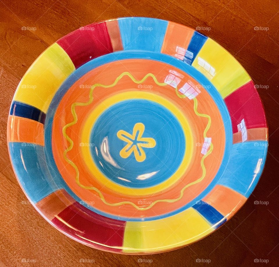 A large, multi-colored festive serving bowl, bursting with vibrant hues of red, yellow, orange, and blue. The bowl’s smooth, rounded shape and rich, glossy finish give it a playful and inviting appearance, enhancing the overall dining experience.