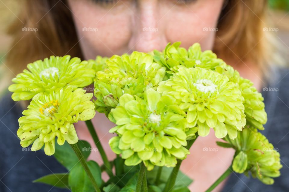 Horizontal closeup photo of a bouquet of green flowers with a blonde Caucasian woman in a grey shirt in soft focus in the background
