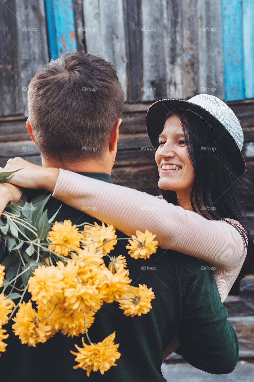 Happy couple in love hugging kissing holding yellow flowers smiling. Woman and man romantic 