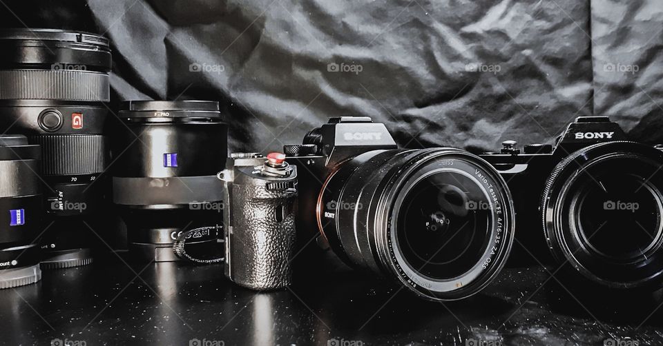 Sony a7ii camera with 16-35mm lens Zeiss lens attached. Sony a7s camera next to a7ii. Zeiss lens  in background. 