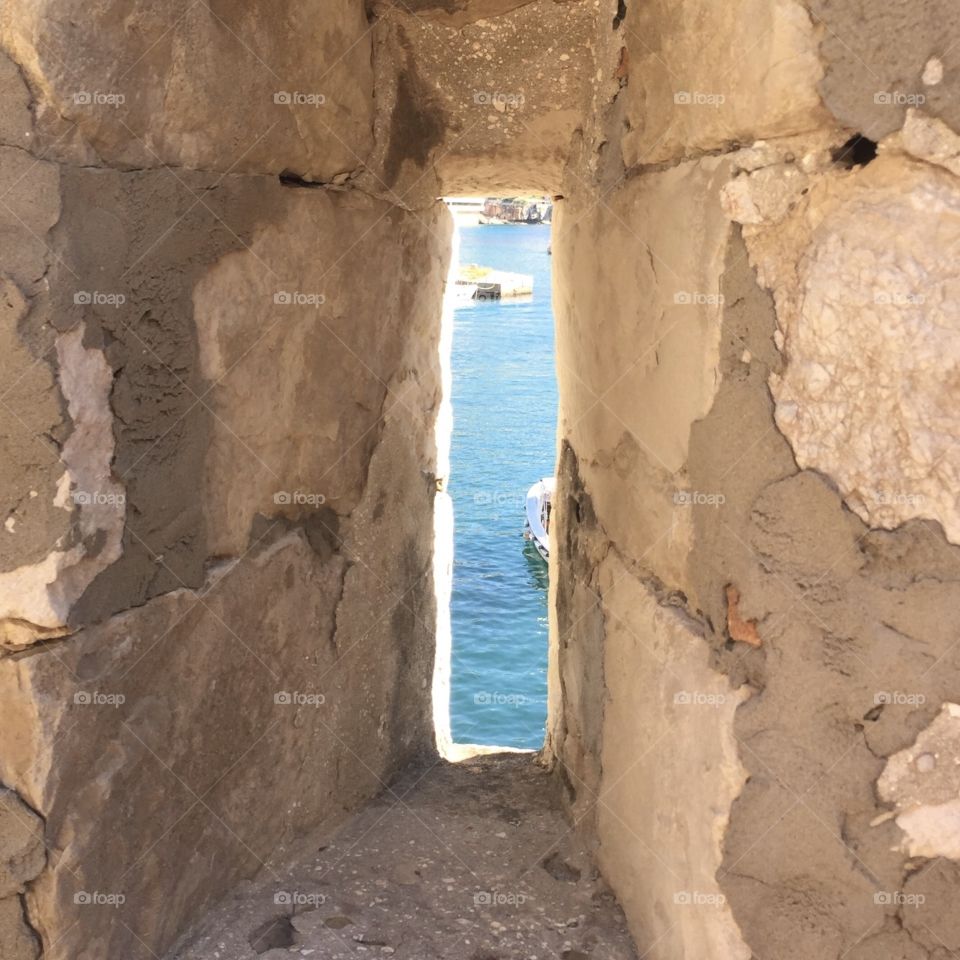 View of the sea ocean through hole in old stone wall 