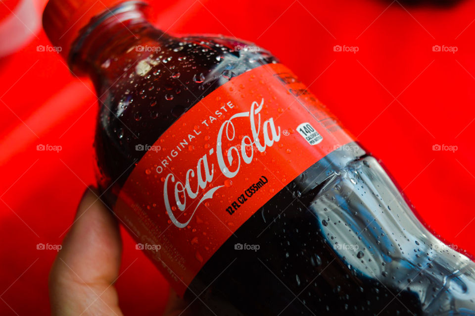 A persons hand holding a plastic bottle of Coca-Cola with condensation on a red background
