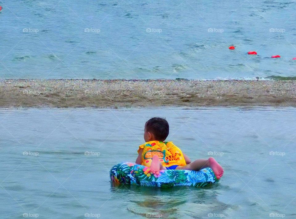 Summer.  Sea.  In the warm water of shallow water, a boy swims on a life buoy