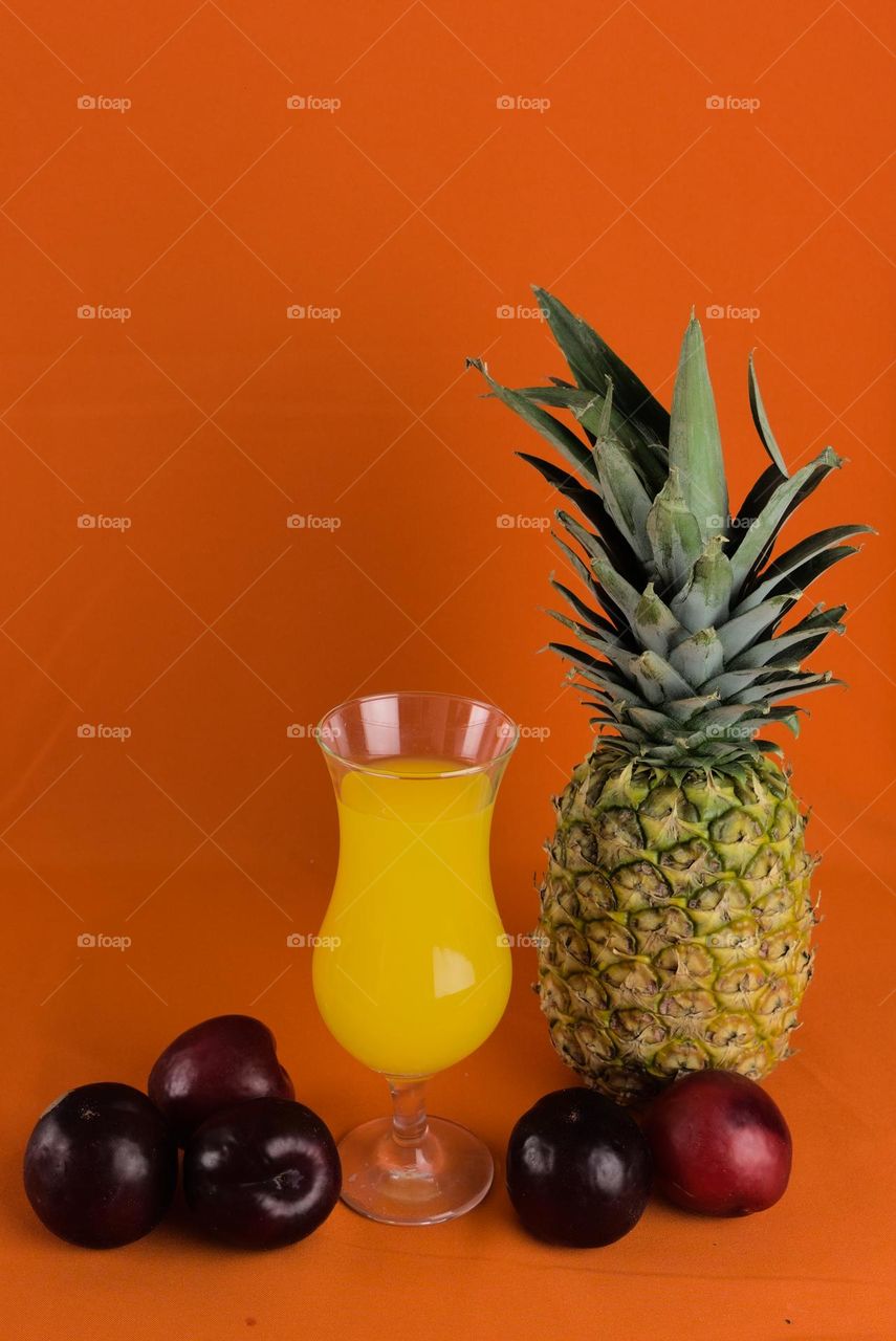 Red plums and crystal glass with natural juice on orange colored background