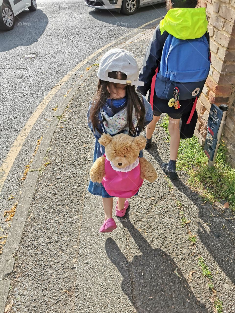Boy and girl walking in the street with Teddy on the girls back and backpack on boy.