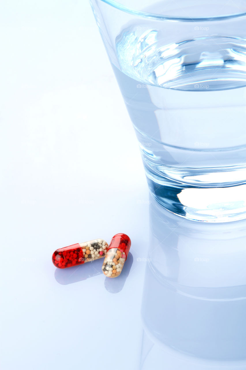 Medicine Capsules and glass on white reflective background