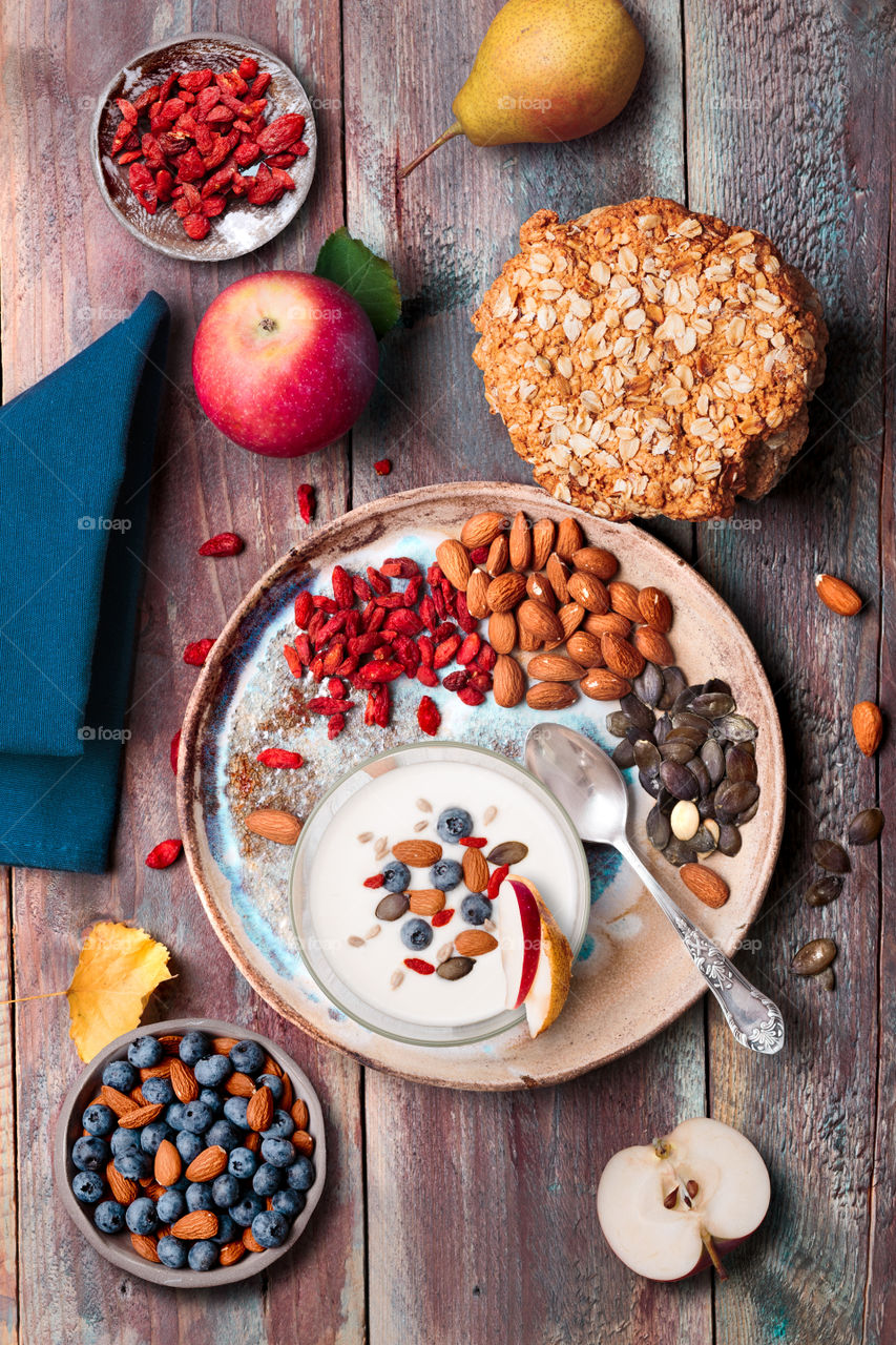 Breakfast on table. Yogurt with added blueberries and roasted almonds. Muesli cookie, apples and pears on wooden table. Light and healthy meal. Good quality balanced diet. Flat top-down composition