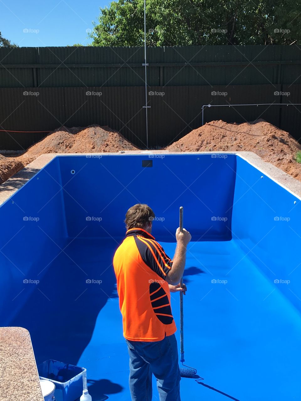 Contractor (male) repairing and repainting fibreglass pool liner blue