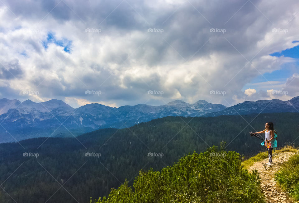 Woman looking at mountain with holding tripod and hiking pole