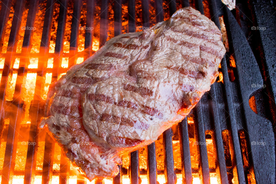 a steak grilling on a red hot infrared grill on a cold day with steam curling up from the meat