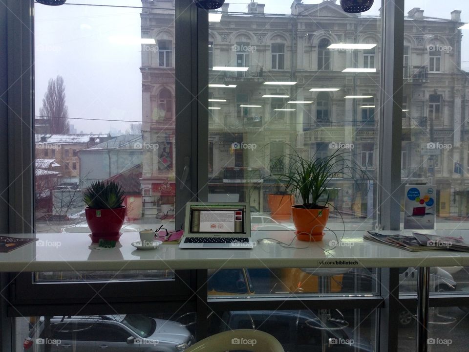 Table at the window with a flower in pot, laptop and a cup of coffee 