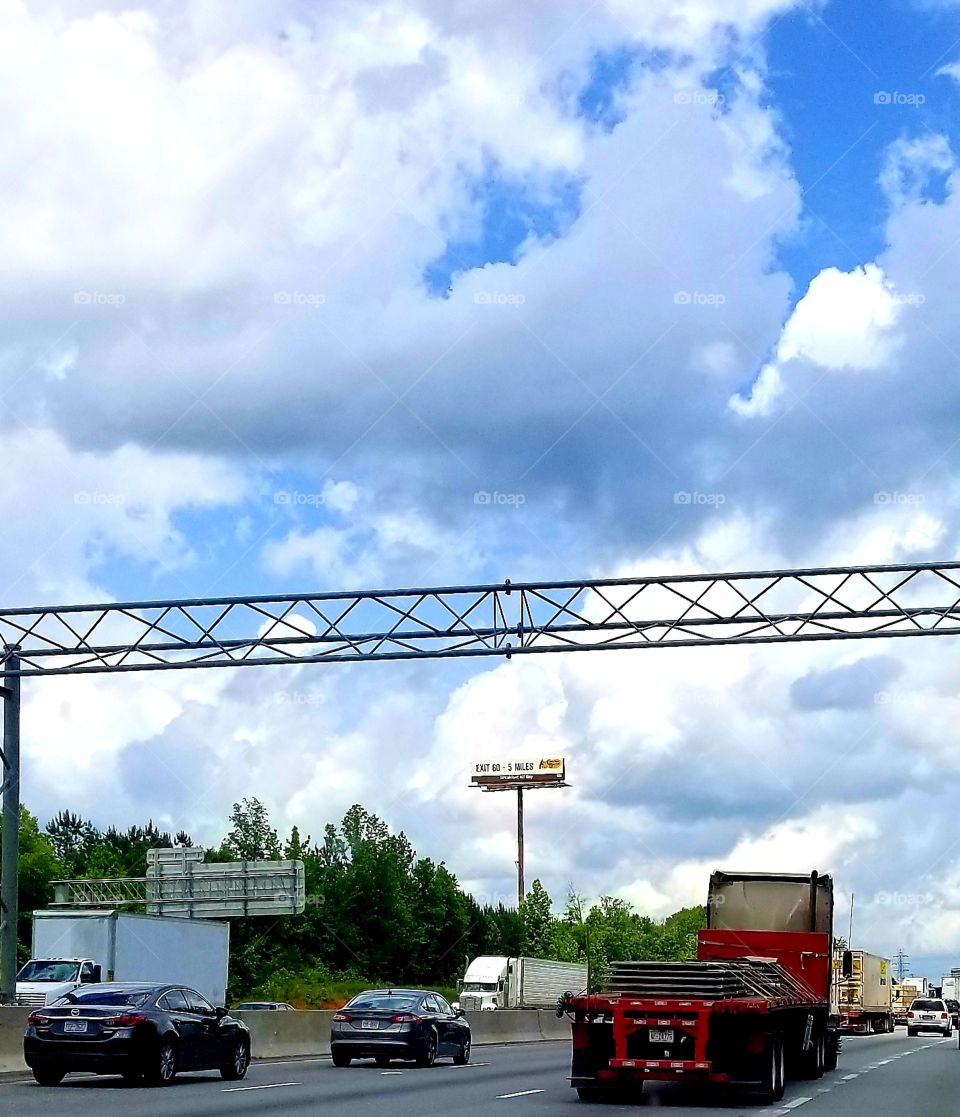 Traffic jam reality of big truck driving in a small car world with blue classic fluffy cloud skies overhead, I85N Concord, North Carolina.