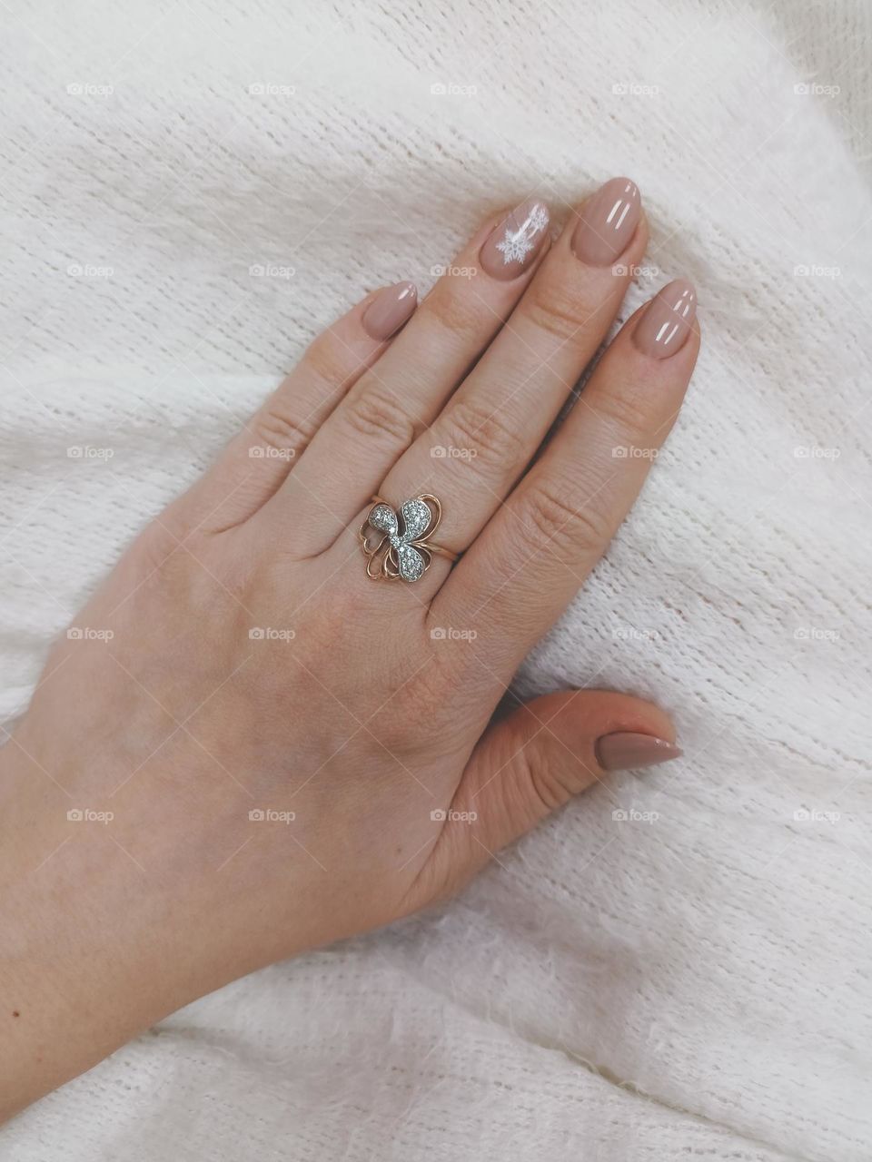 manicure on a female hand, the color of nails is coffee with milk, a white snowflake, female hands on a white background, a warm fluffy scarf, nail polish, a gold ring on a finger, a female hand with a ring