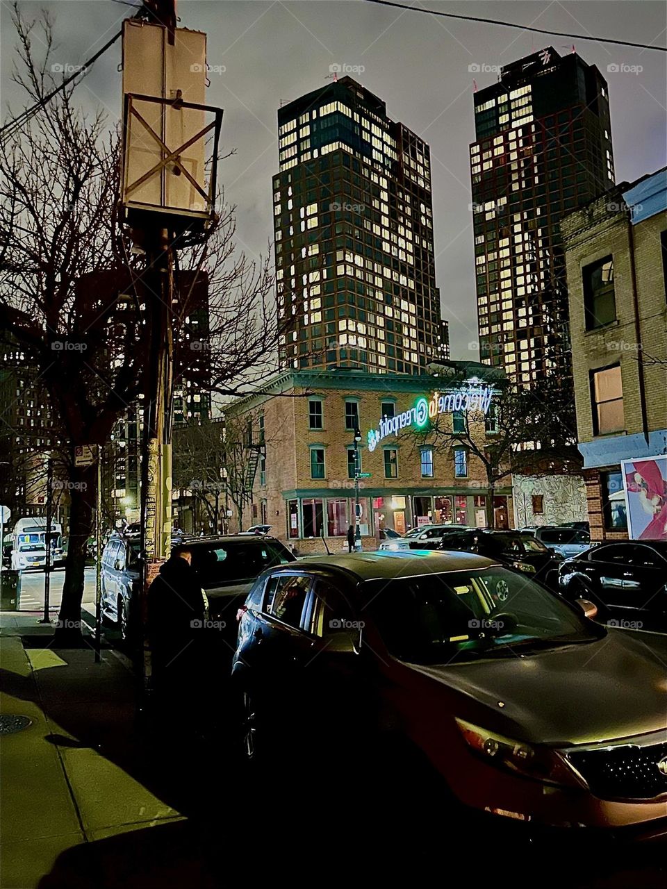 This is the intersection of “Manhattan Ave” and “Box Street” in “Greenpoint”, Bklyn with festive illumination. “Welcome to Greenpoint” including a comet star is the inscription of the fluorescent sign that spans the street. 2023. Hypnotic Productions