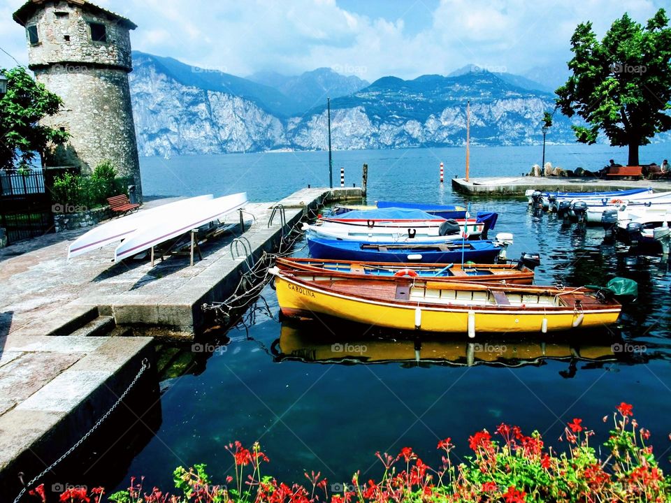 Brenzone sul Garda Harbour with Tower, red flowers in the foreground and view across the lake and mountains in the background