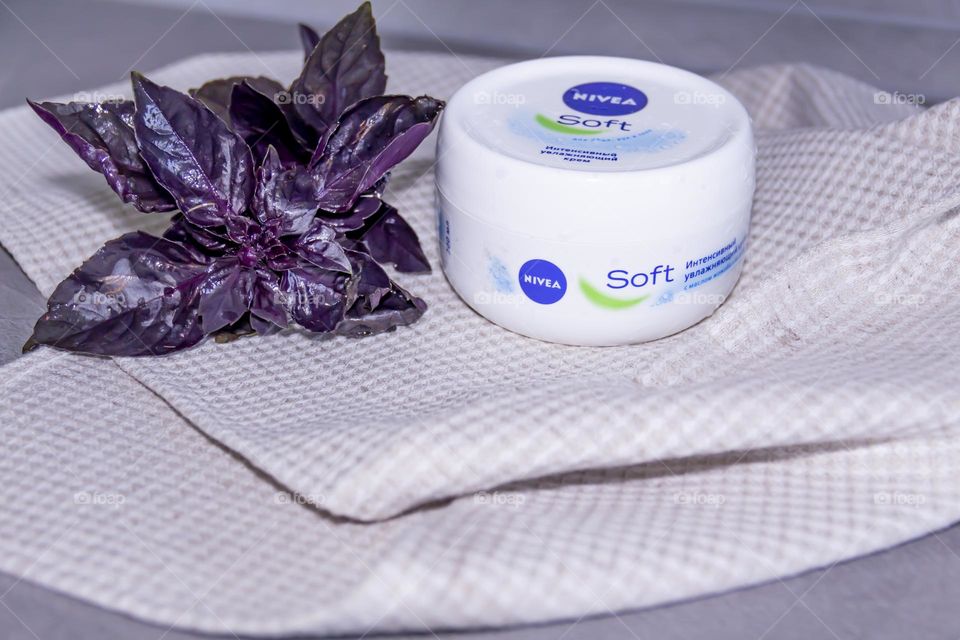 Cosmetic product, Nivea skin care cream on a gray surface and a linen napkin and a sprig of purple basil.